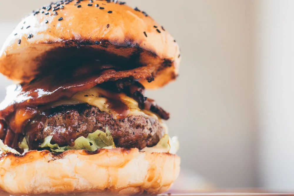 Layers of a burger with cheese, bacon, lettuce, and a sesame bun