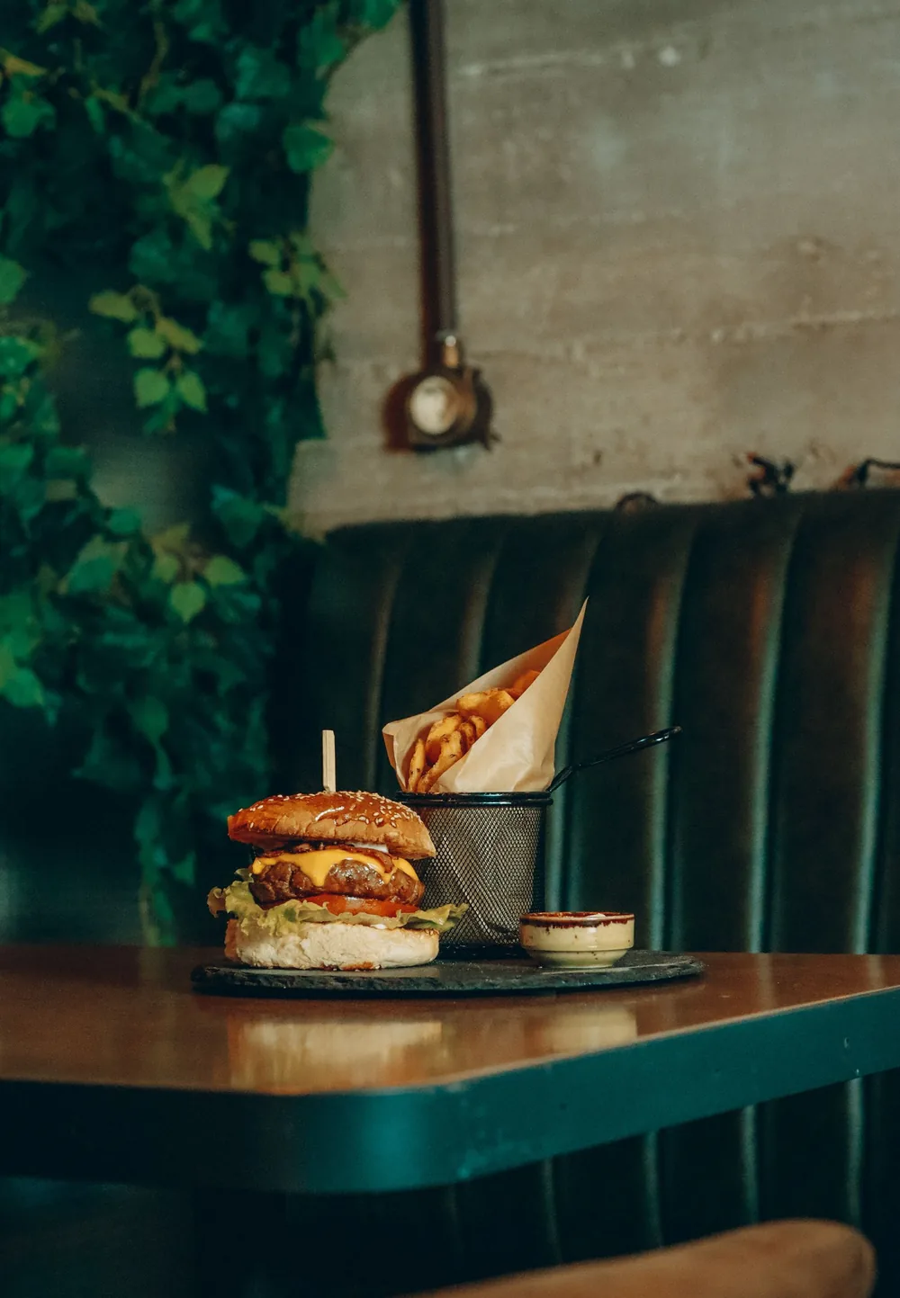 Burger and fries on a restaurant table by a teal upholstered booth